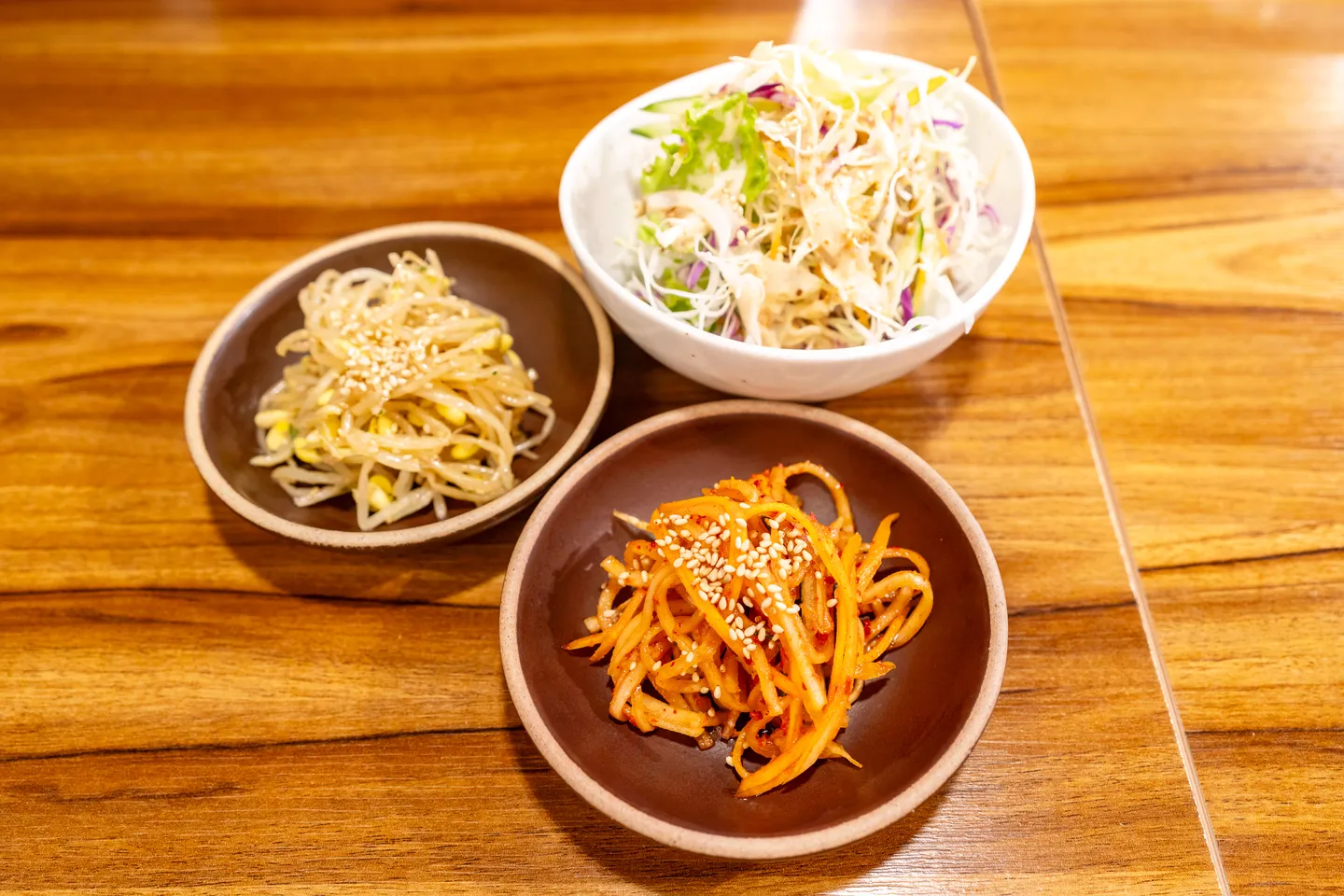 Beilagen im Stil eines koreanischen Restaurants werden serviert: geraspelter Rettich, gewürzte Sojabohnensprossen und Krautsalat.