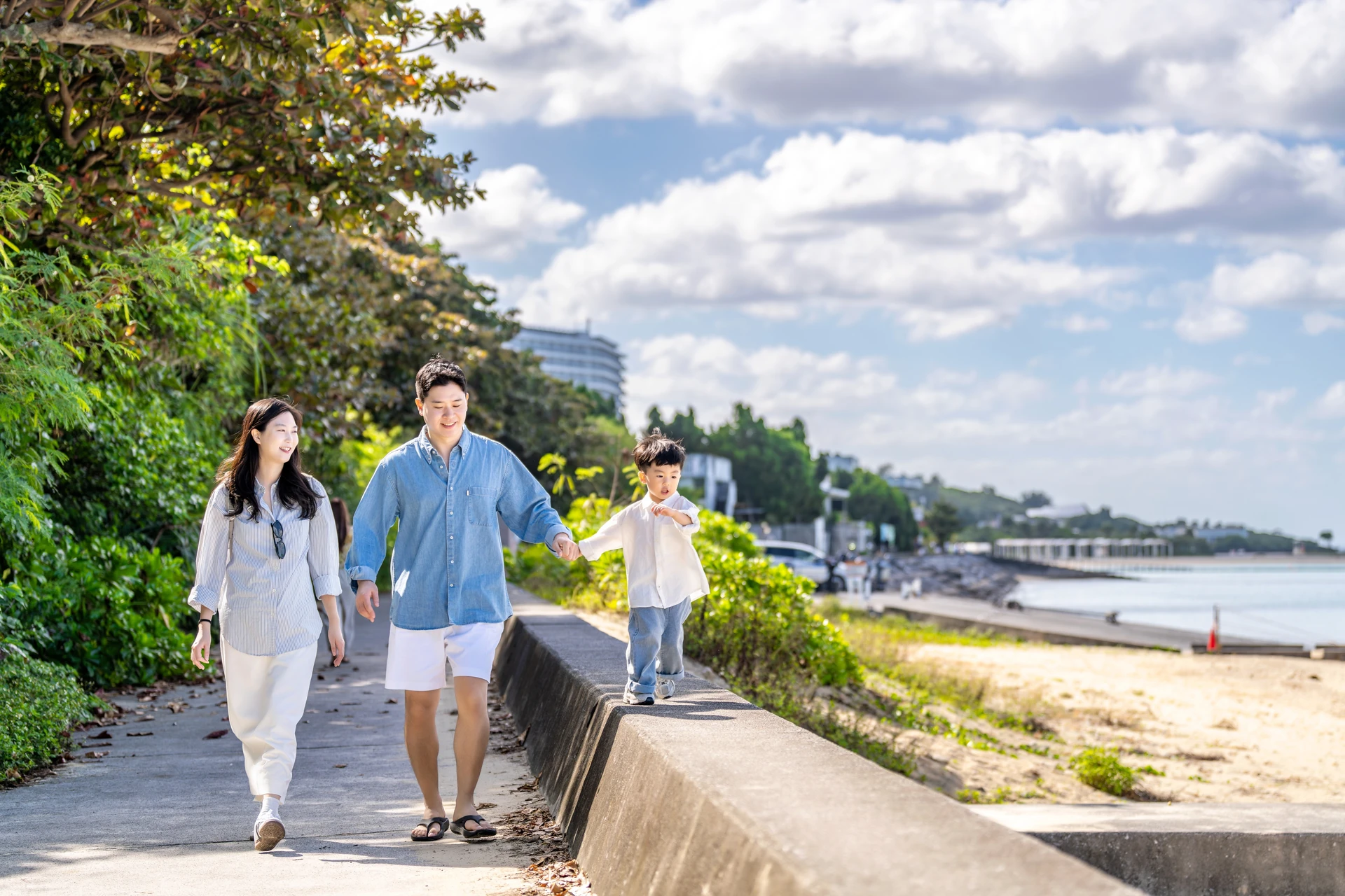해안 산책로의 낮은 담을 따라 아이 손을 잡고 걷는 가족