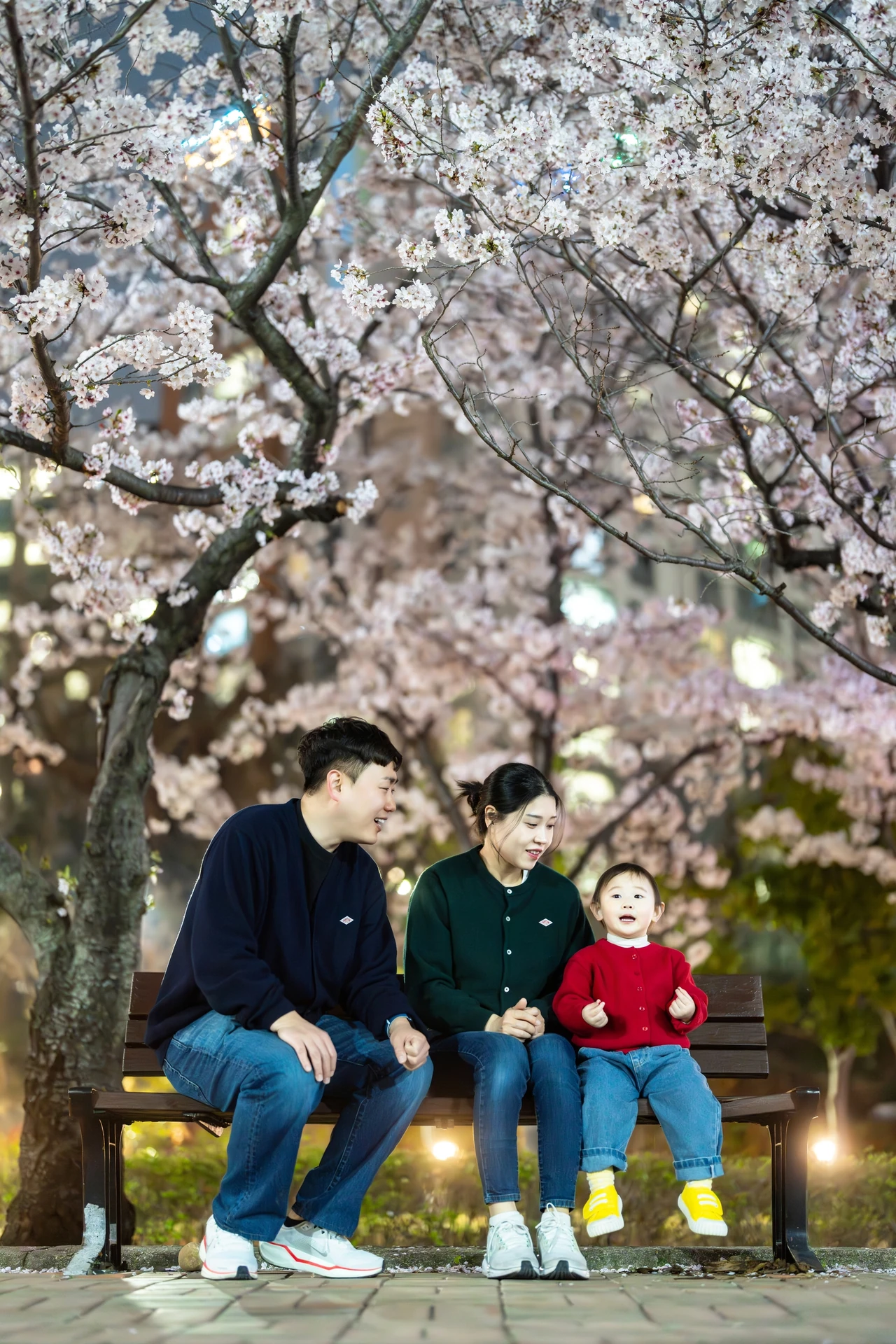 벚나무 아래 벤치에 나란히 앉은 가족 세 명