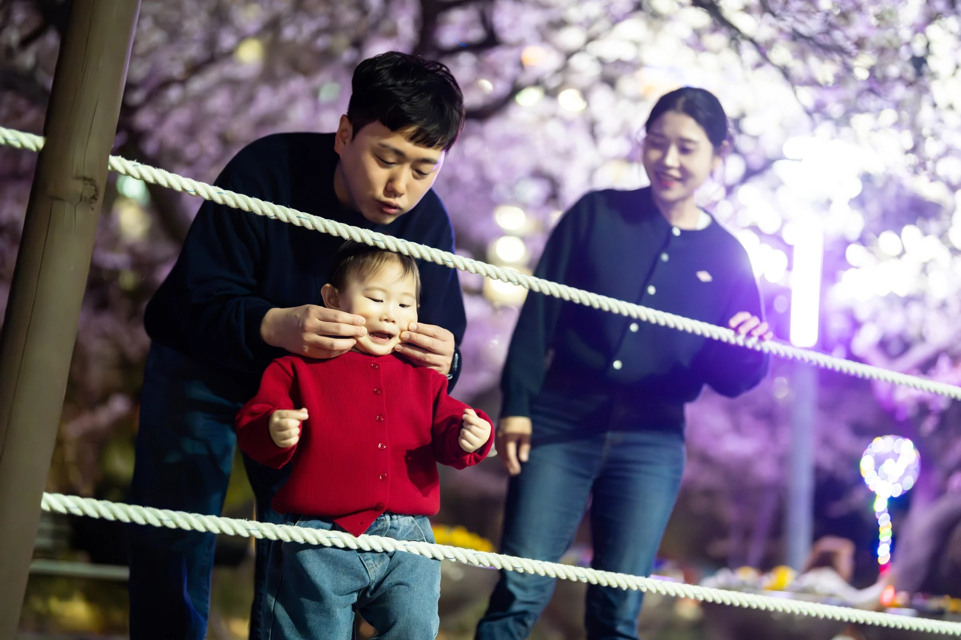 밧줄 울타리 앞에서 볼을 잡는 아기와 엄마 아빠