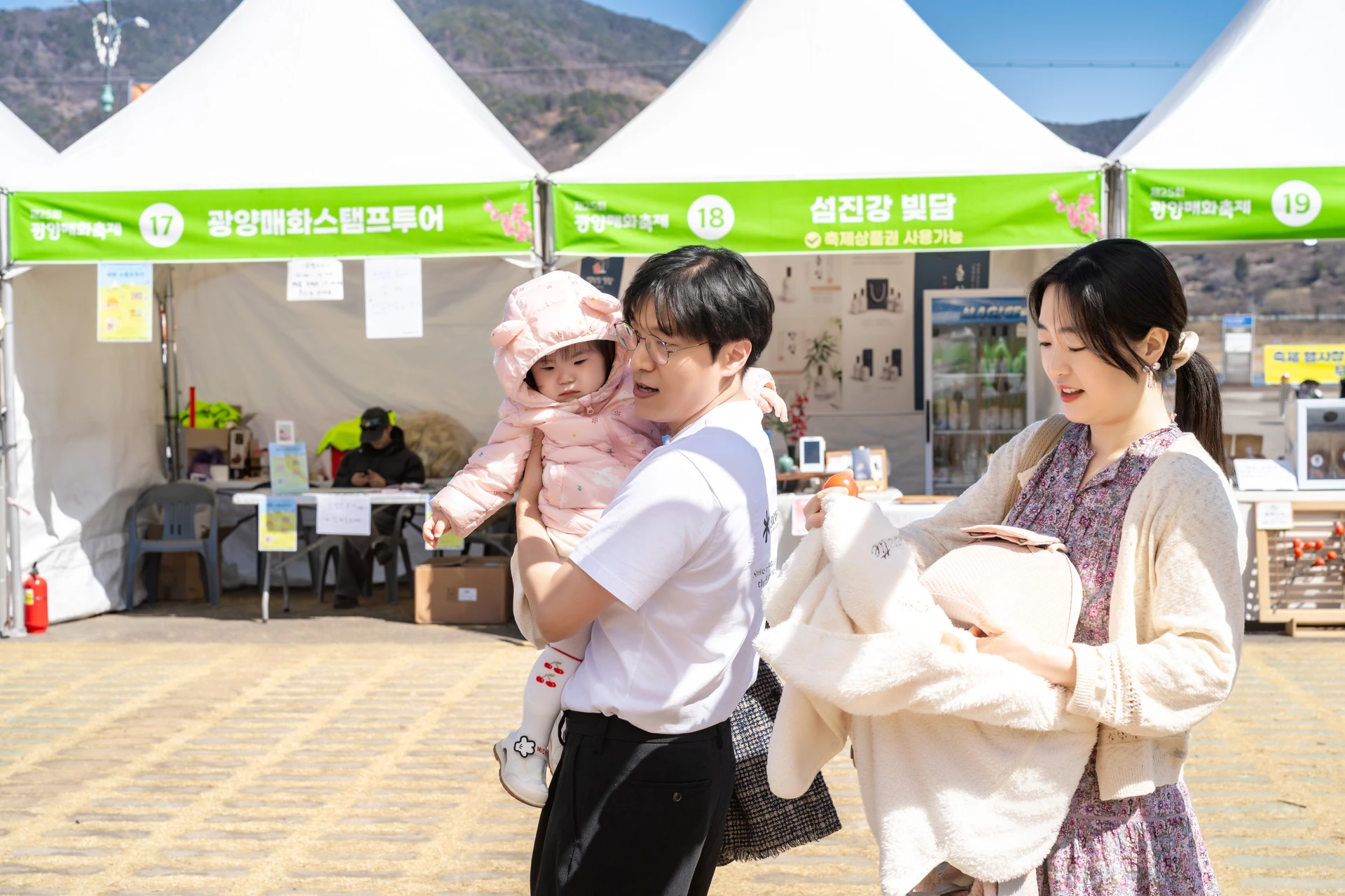 축제 천막 앞에서 아기를 안은 아빠와 엄마