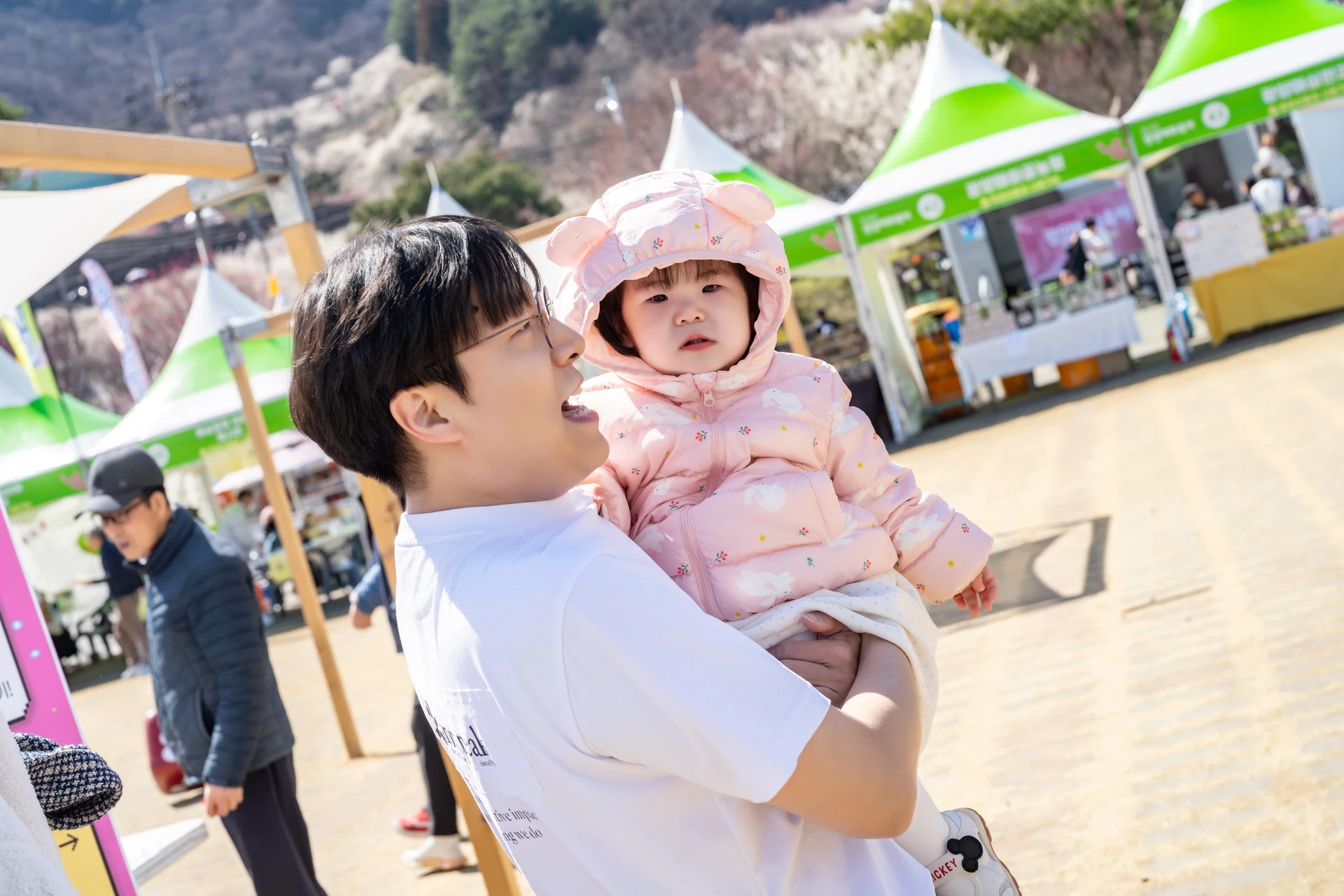아기를 안고 웃는 아빠와 뒤로 보이는 축제 천막