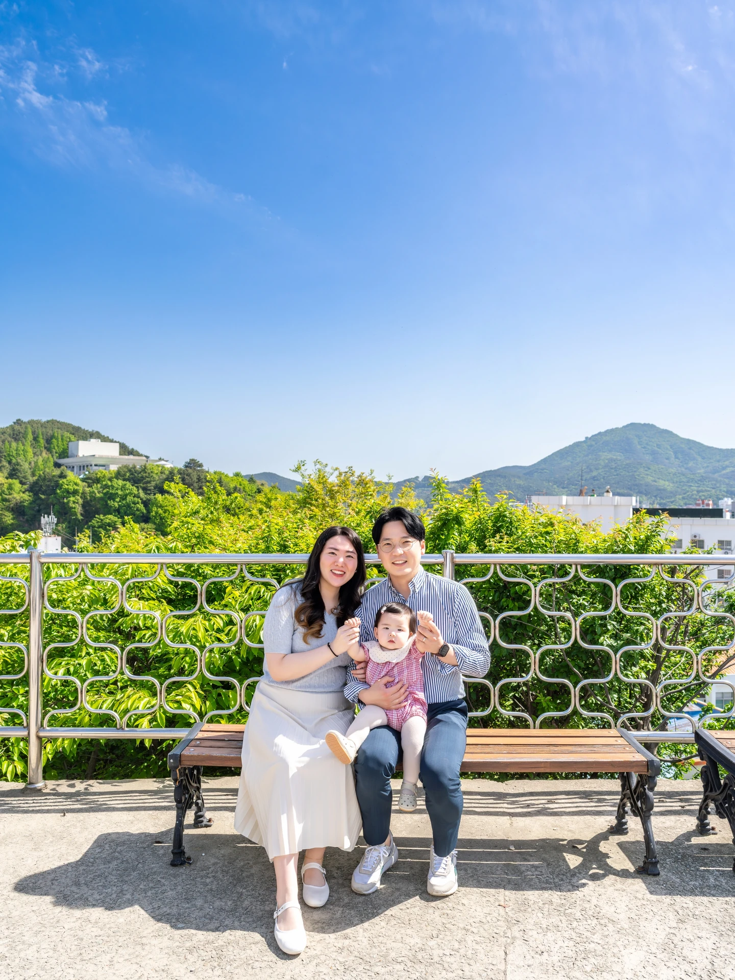 동피랑 전망 벤치에 아기와 함께 앉은 부부와 멀리 보이는 통영의 산