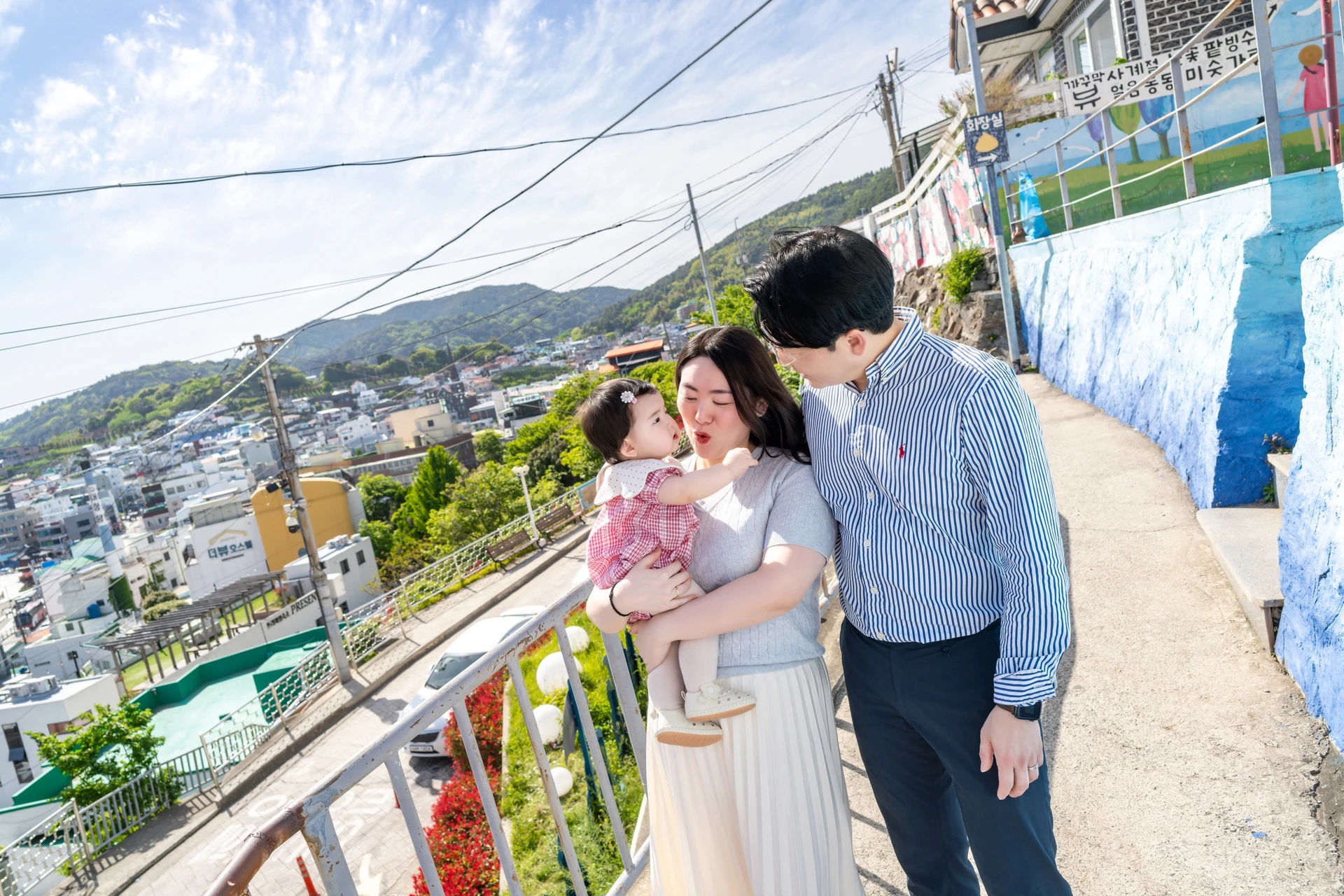 벽화 담장 옆 길에서 아기를 안고 서로 바라보는 부부