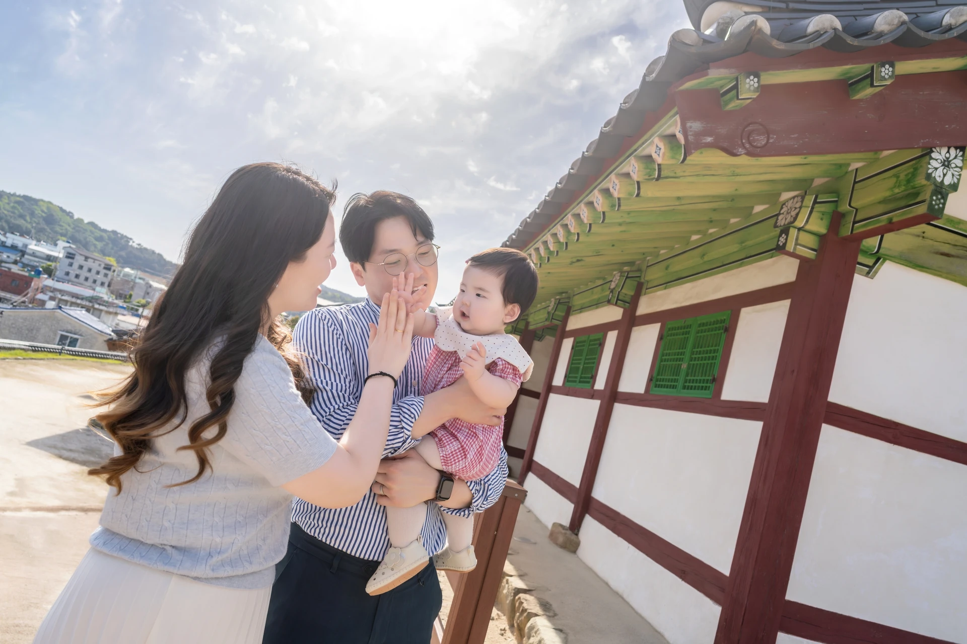 세병관 흰 벽과 기와 앞에서 아기를 안고 아기를 바라보는 부모